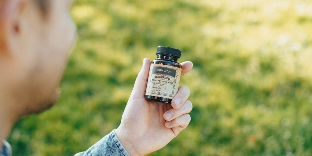 closeup man's hand holding CBD product bottle